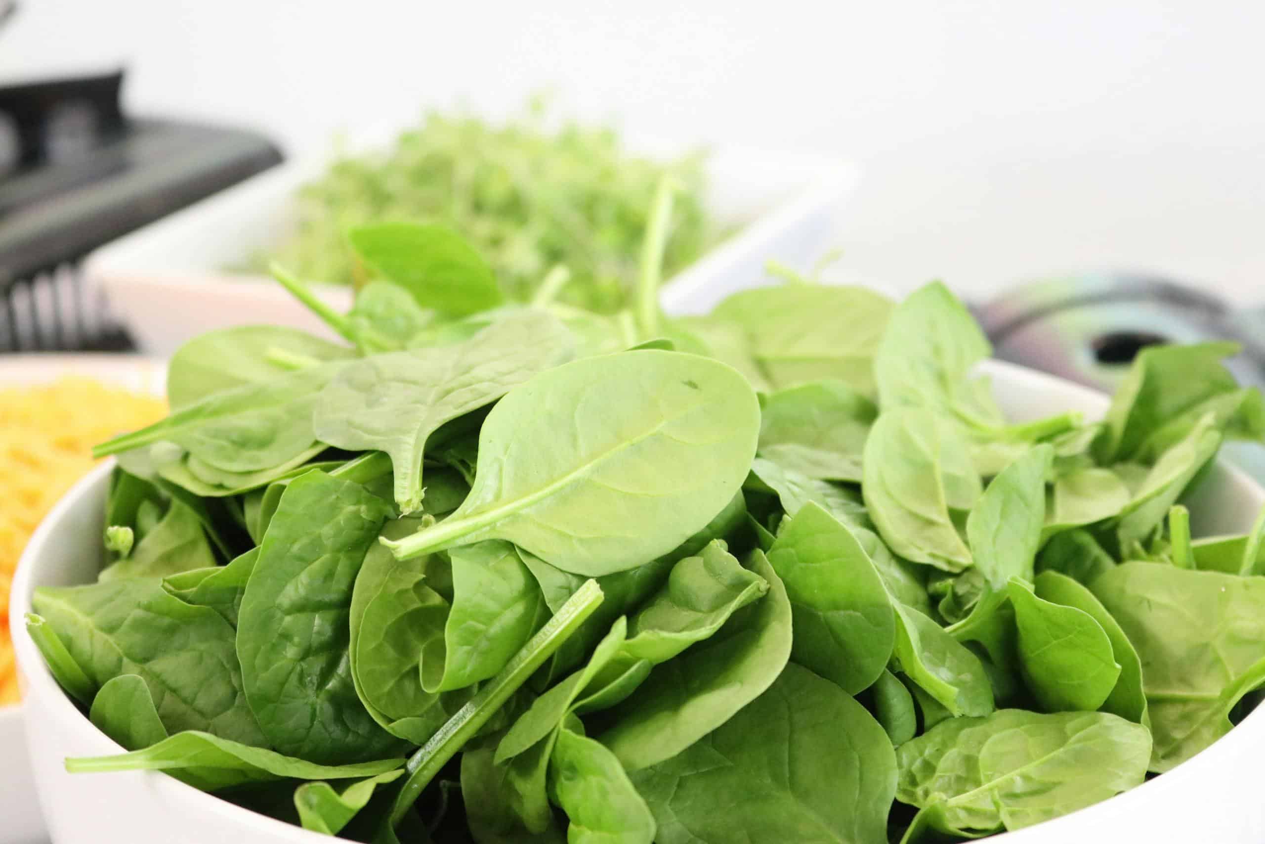 A close-up of fresh spinach leaves in a white bowl, ideal for healthy salads.