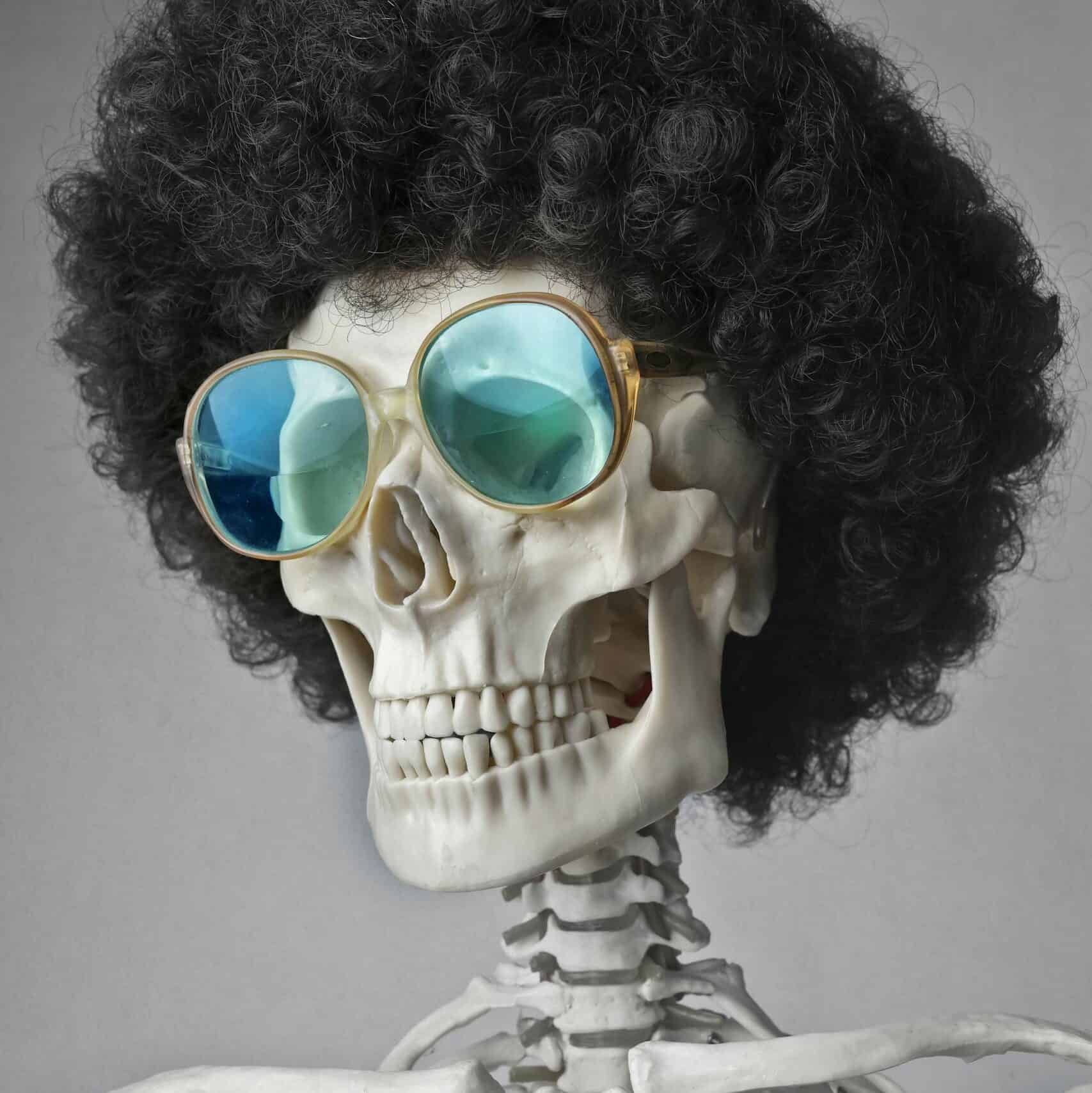 A skeleton wearing an afro wig and sunglasses, set against a gray background.