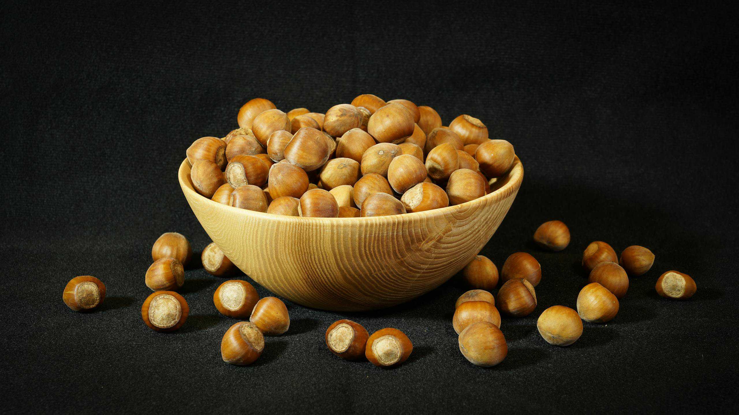 A wooden bowl filled with hazelnuts on a dark background, perfect for food photography and culinary themes.