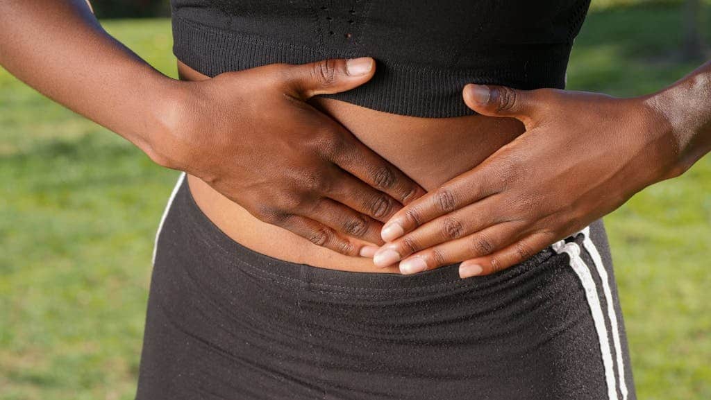 Close-up of a person holding their stomach, indicating abdominal pain outdoors.