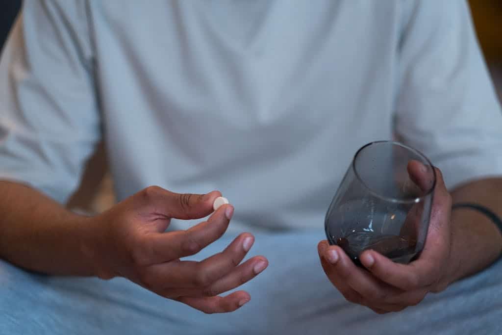 Close-up of an unrecognizable man taking a pearl powder with a glass. Indoor setting.