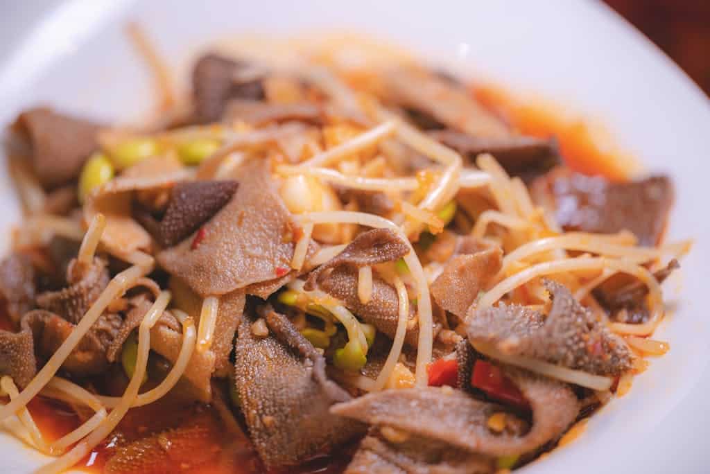 Close-up of spicy Asian stir-fried tripe with bean sprouts served on a white plate.