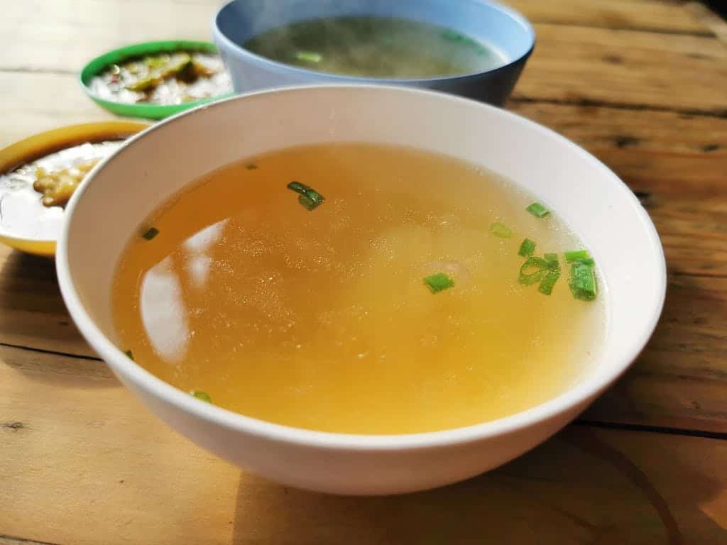 Delicious homemade soup , made with beef bones, garnished with scallions in a bowl on a rustic wooden table.