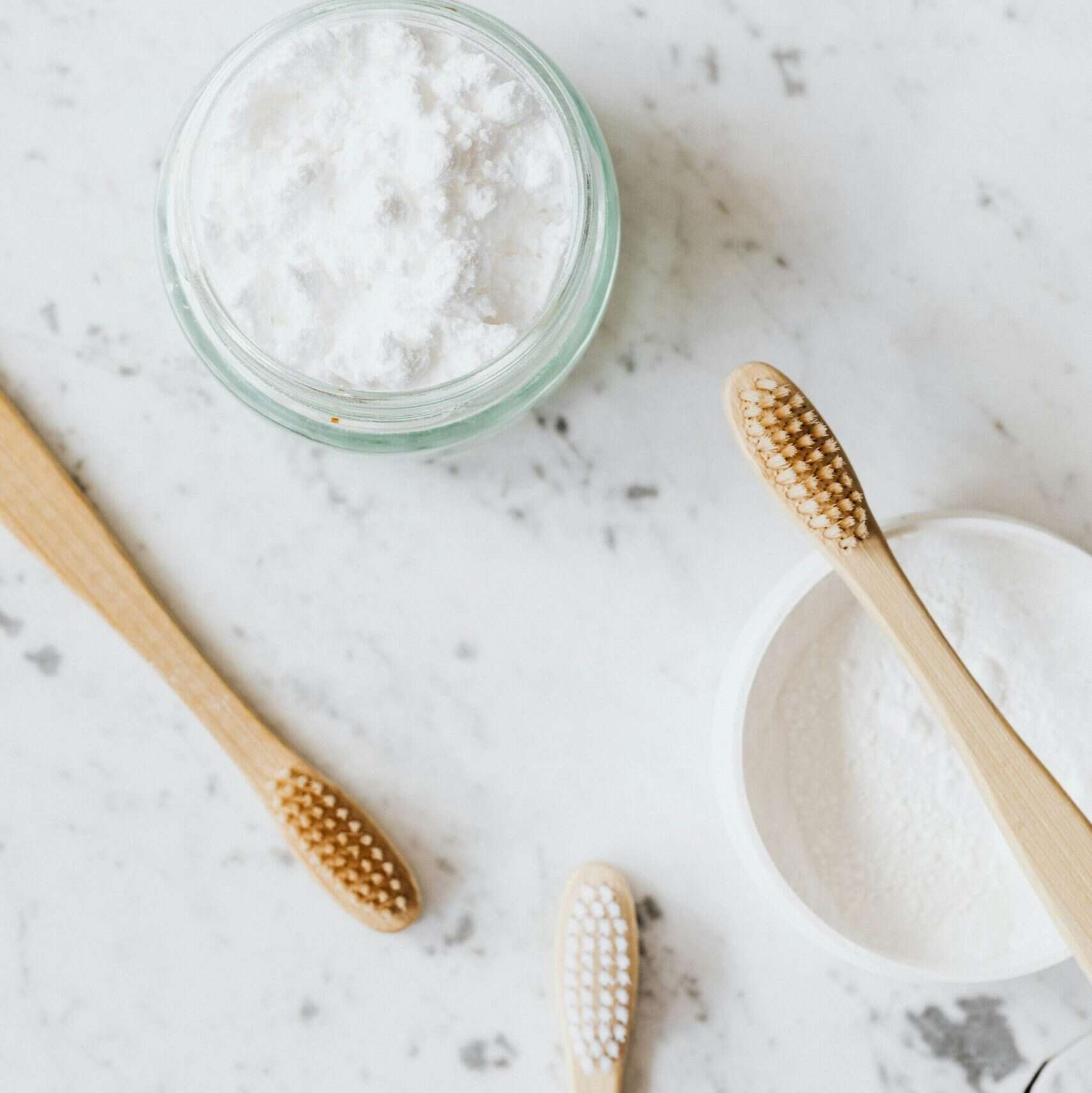 From above of glass and plastic jar with white tooth pearl powder near wooden toothbrushes on marble table with grey lines and crack