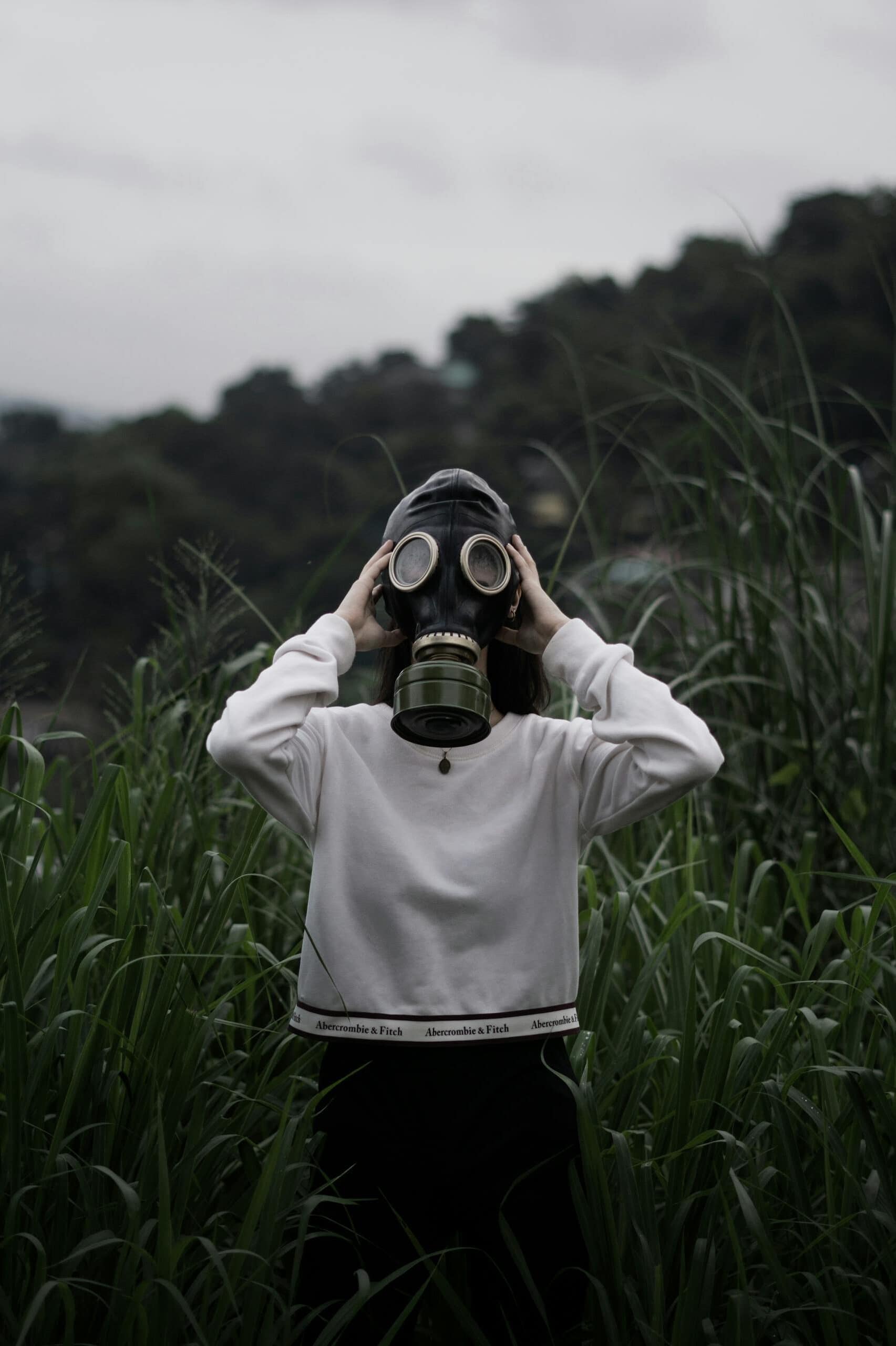 Individual wearing a gas mask standing in tall grass, symbolizing protection from toxins.