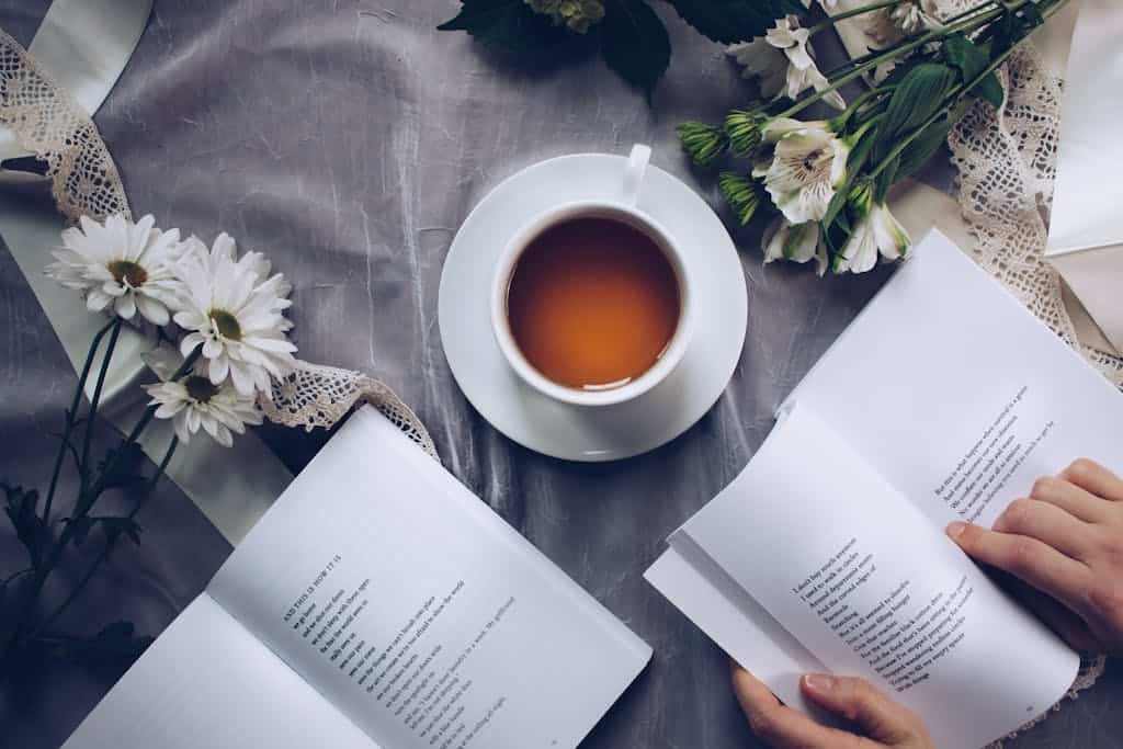 Inviting cozy reading setup with tea, poetry books, and fresh flowers on a table.