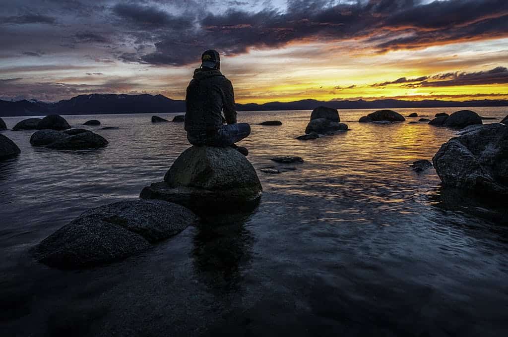 Silhouette of a man seated on rocks, gazing at a serene Lake Tahoe sunset.