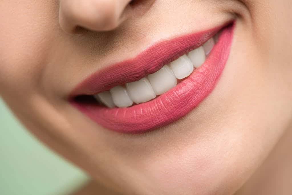 Vivid close-up image of a woman's smile showcasing red lipstick and white teeth on a light background.