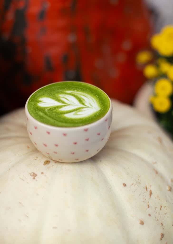 Warm matcha latte with latte art sitting on a pumpkin, evoking cozy autumn vibes.