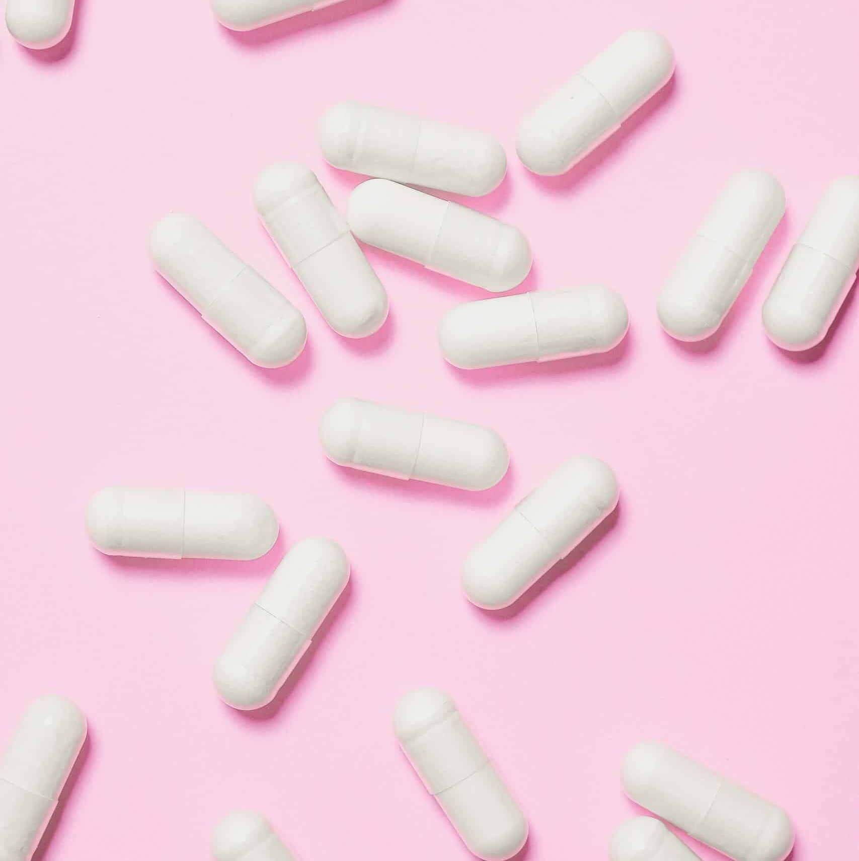 White medicinal capsules scattered on a vibrant pink background, symbolizing healthcare and wellness.