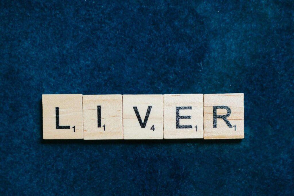 Wooden Scrabble tiles spelling 'Liver' on a textured dark blue background.