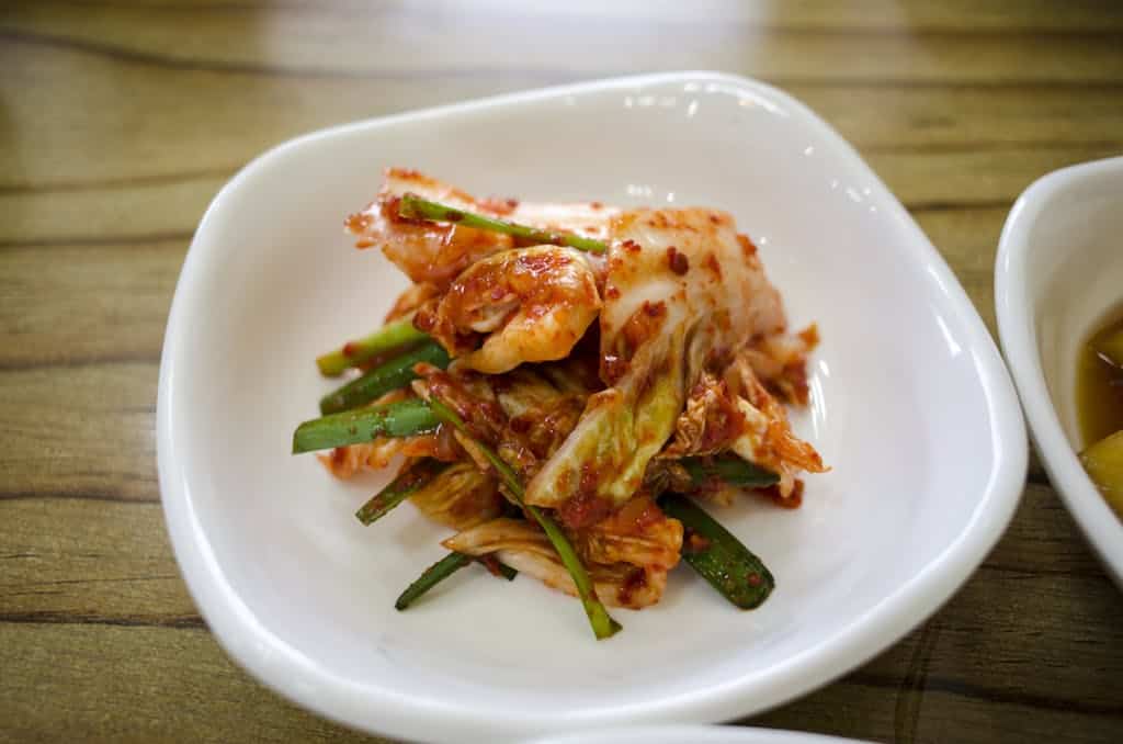 Close-up of traditional Korean kimchi served in a white ceramic dish on a wooden table.